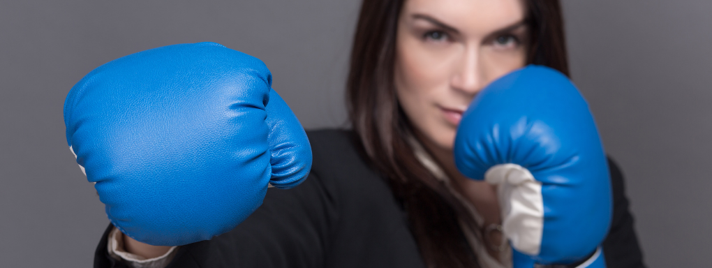 Female business woman with blue boxing gloves punching towards the camera