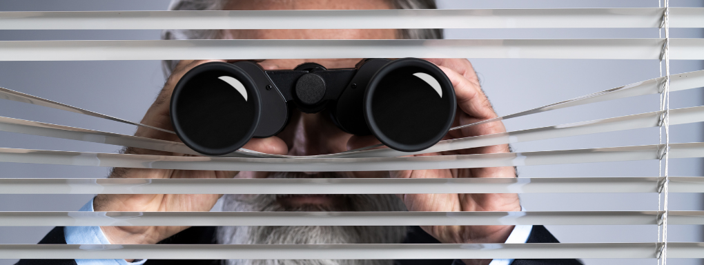 Man looking through horizontal blinds with binoculars