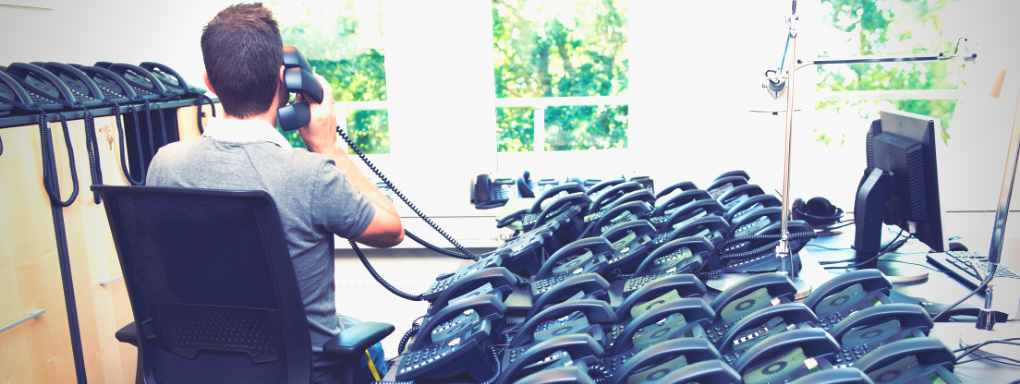 Man with hundreds of old corporate telephones sat on his desk