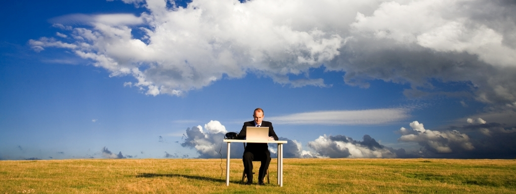 Man sitting at a desk in an empty field with blue skies 